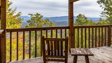 Une terrasse en bois avec une chaise et une table en bois, offrant une vue sur un paysage montagneux aux couleurs automnales.