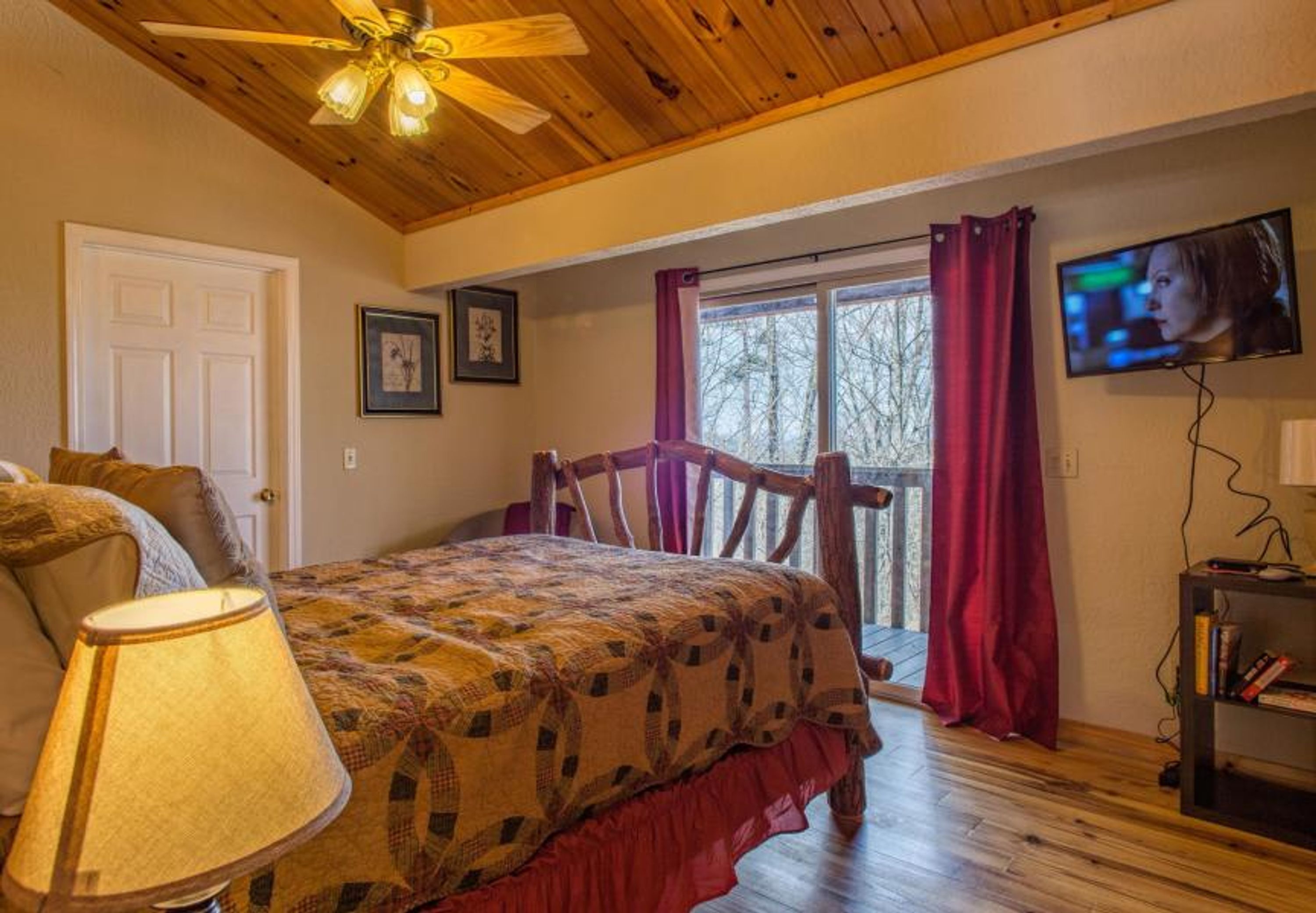Un dormitorio con cama, ventilador de techo, televisión y ventana con cortinas.