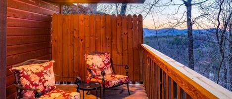 Une terrasse en bois avec deux chaises et une table, offrant une vue sur un paysage montagneux.