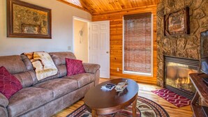 A cozy living room with a stone fireplace, wooden ceiling, and a comfortable couch with throw pillows. - Greatview Pooltable Hottub Privacy Fireplace (Sevierville)