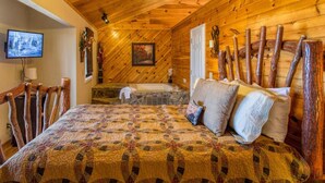 A log cabin bedroom with a bed, a ceiling fan, a television, and rustic decor. - Greatview Pooltable Hottub Privacy Fireplace (Sevierville)