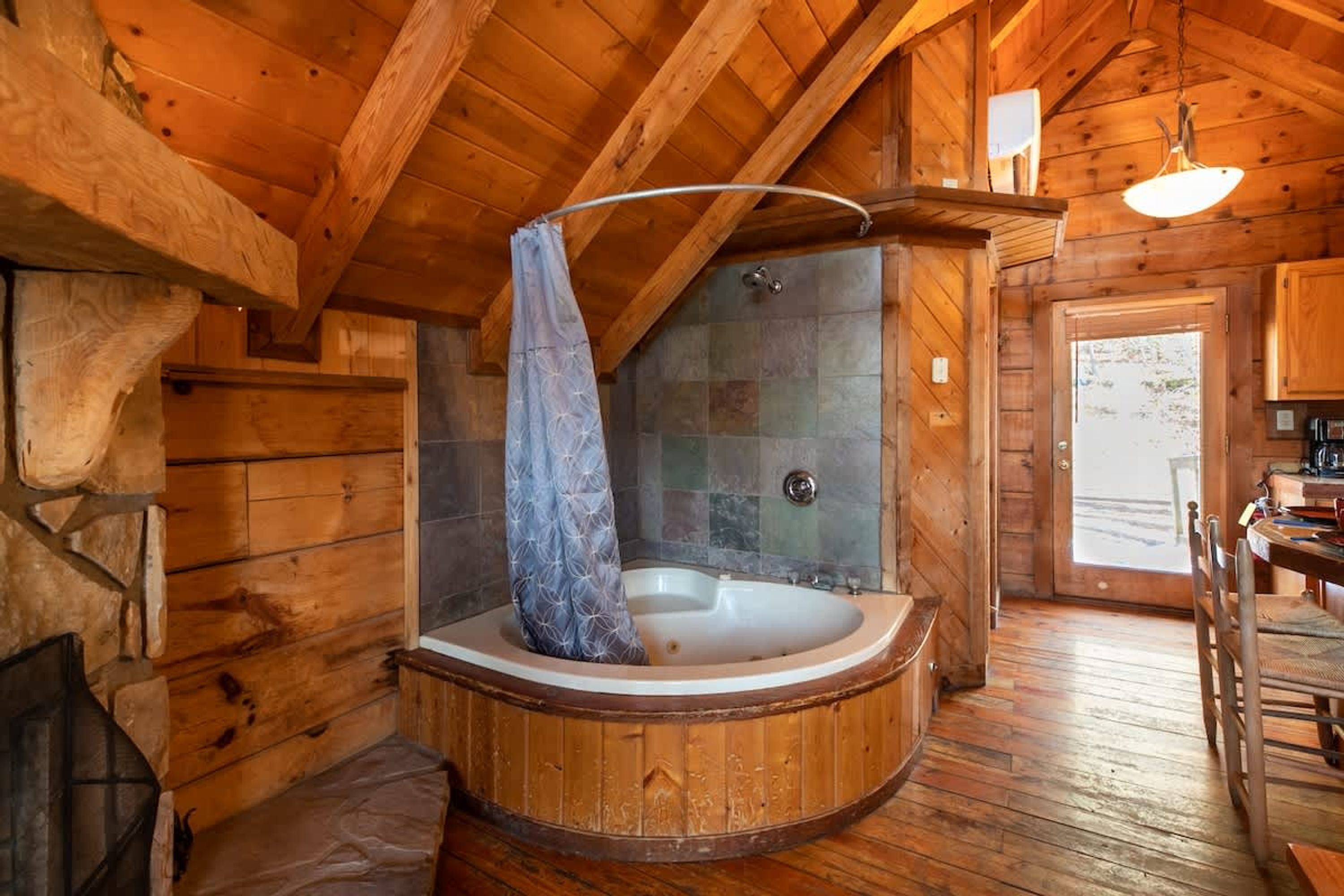 Interno di una baita di legno con camino in pietra, vasca da bagno in legno e cabina doccia in pietra.