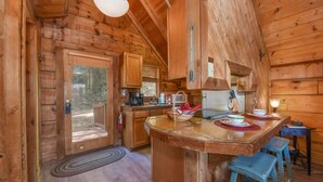 Ein Holzblockbau-Innenraum mit Küchenbereich, Holzsäulen, einer Bar und blauen Hocker.