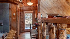 Ein rustikales Holzinterieur mit hohen Decken, Kamin, Essbereich und Blick ins Freie.