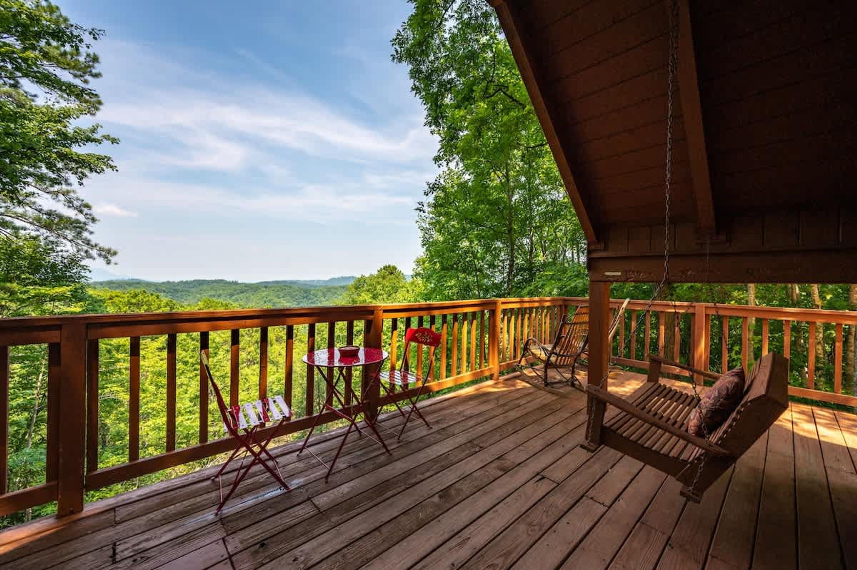 Une terrasse en bois avec un fauteuil suspendu et une table, offrant une vue sur un paysage verdoyant et luxuriant.