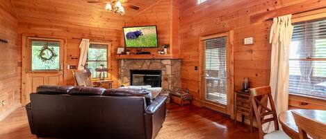 A cozy cabin interior with a stone fireplace, a leather sofa, a television, and wooden walls.