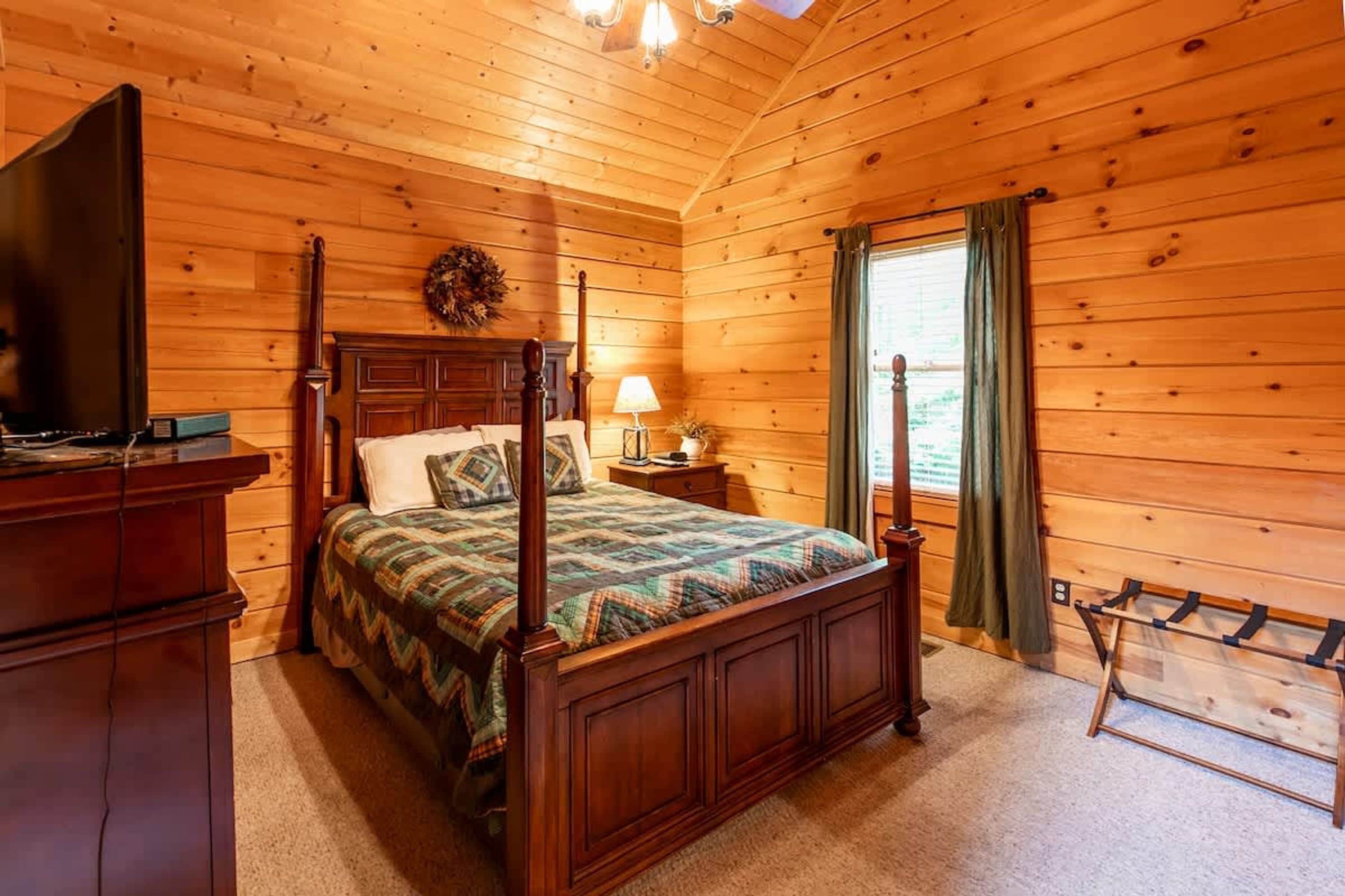 A wooden cabin bedroom with a four-poster bed, a television, a lamp, and a coat rack.