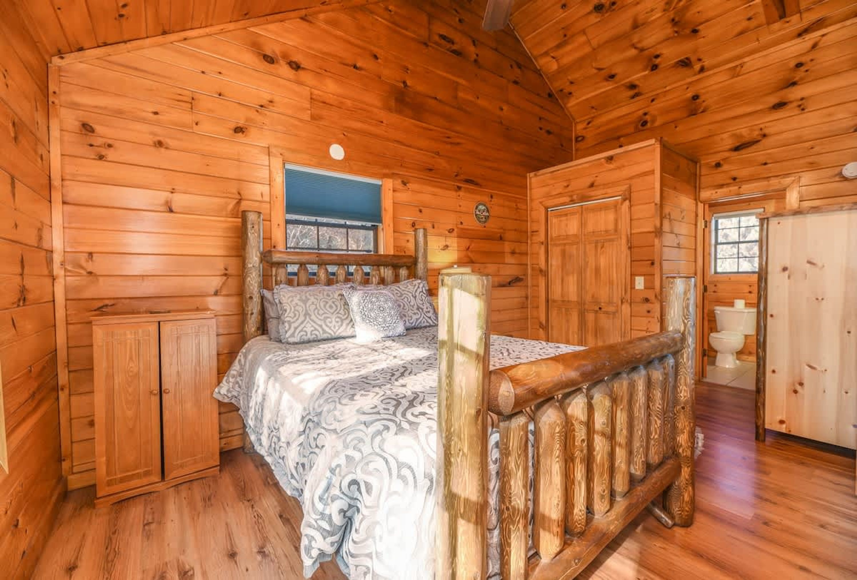 A wooden cabin bedroom with a bed, a wooden wardrobe, and a bathroom.