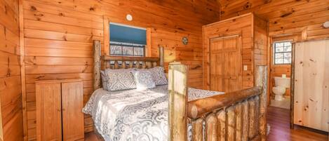 A wooden cabin bedroom with a bed, a wooden wardrobe, and a bathroom.