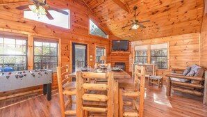 A wooden cabin interior with a dining table, chairs, a foosball table, a television, and a fireplace. - Secluded Cabin Near Smoky Mountains Hot Tub Honeymoon (Sevierville)