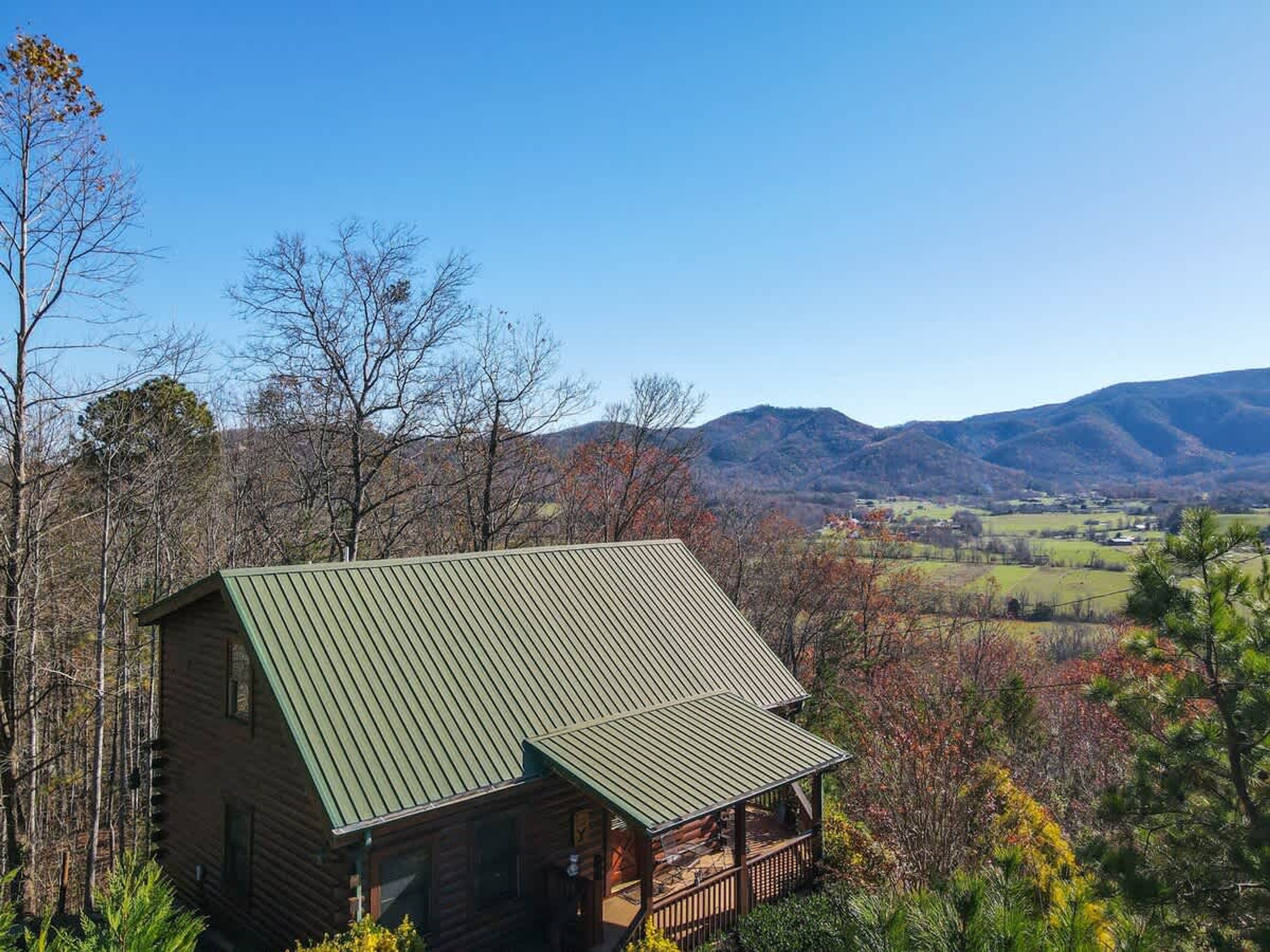 A log cabin with a green metal roof, surrounded by trees and a mountainous landscape.