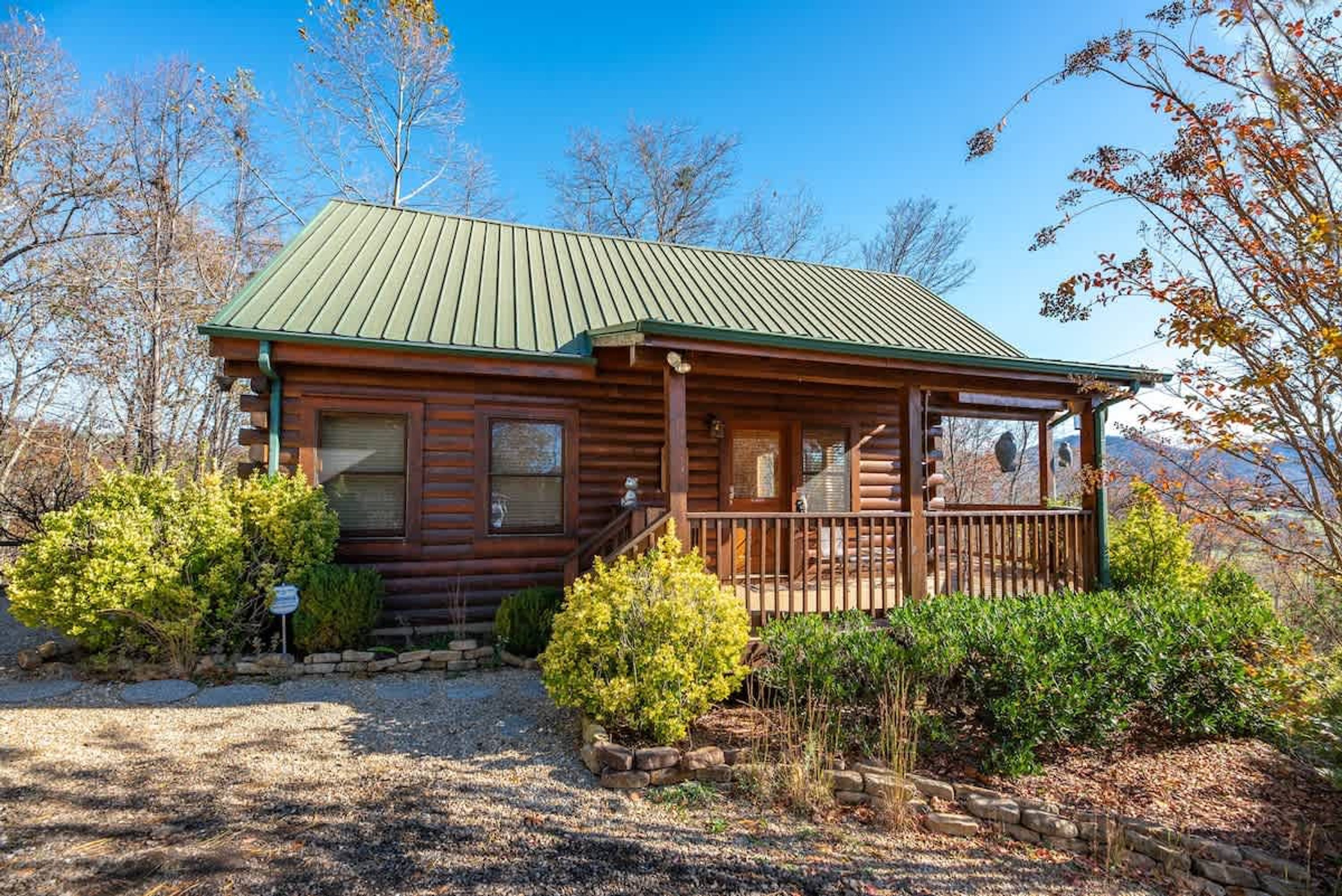 A log cabin with a porch, surrounded by trees and shrubs.