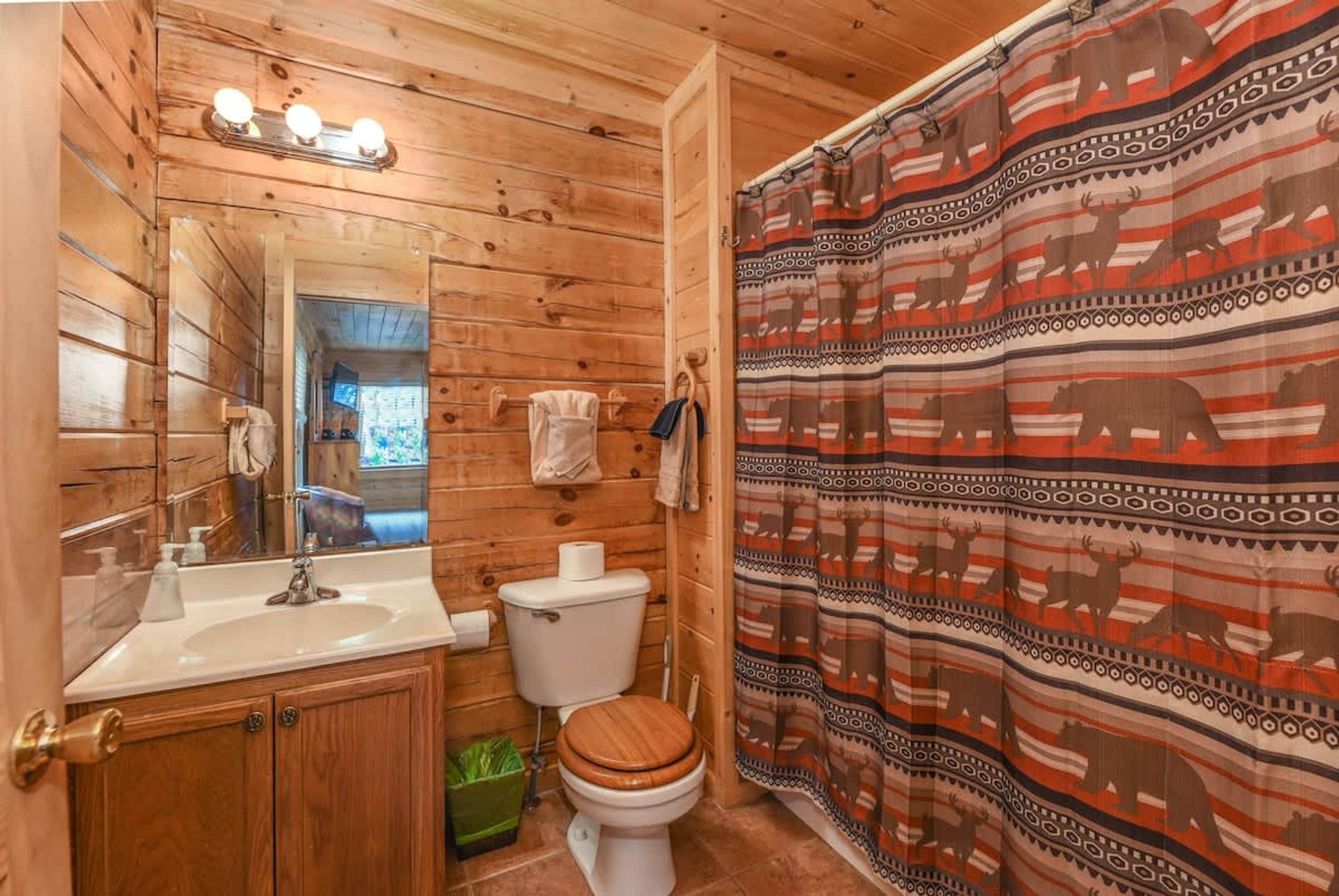 A wooden cabin bathroom with a sink, toilet, and shower curtain featuring animal patterns.