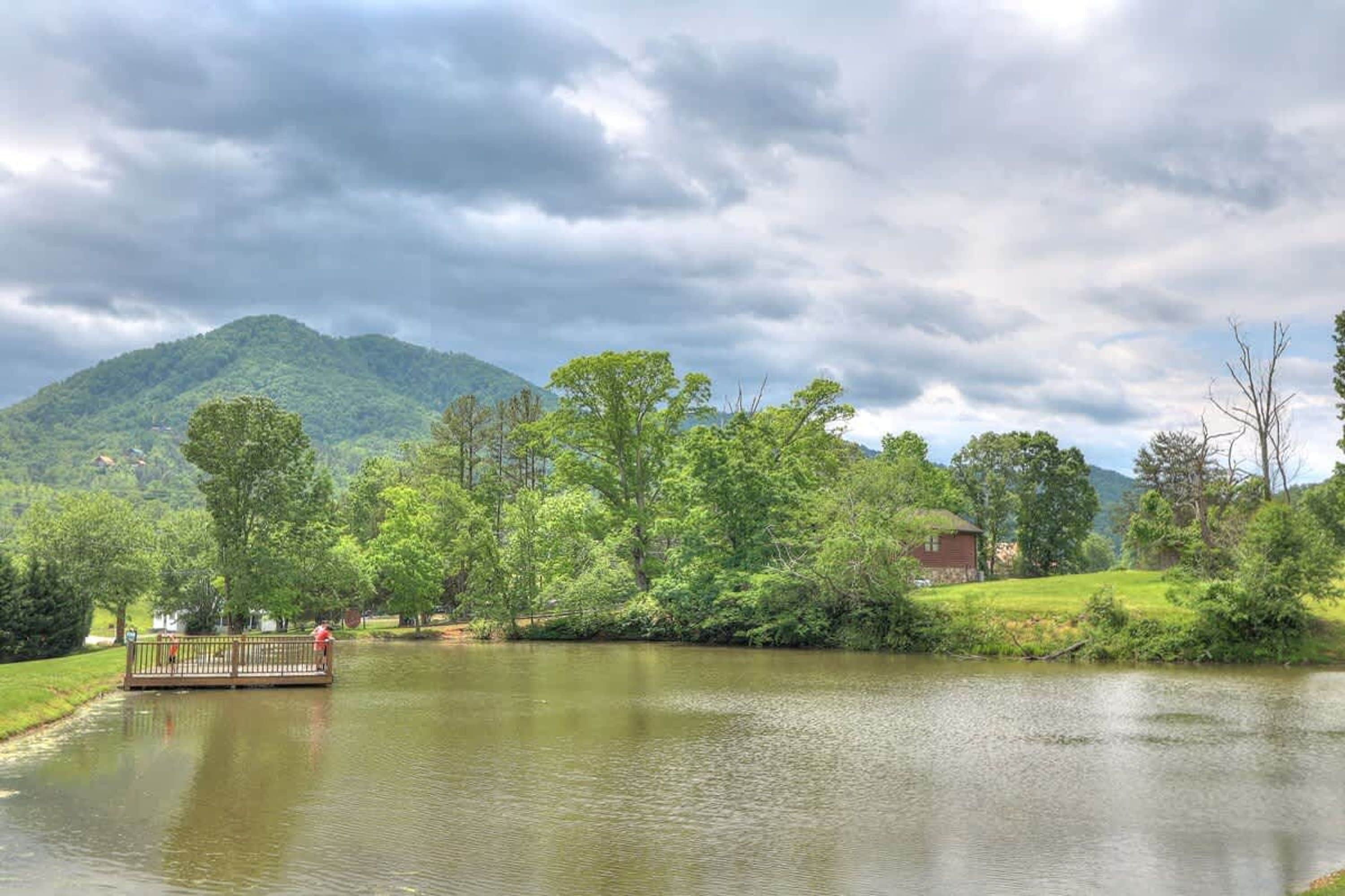 A calm lake with a wooden dock and a small house in the background.