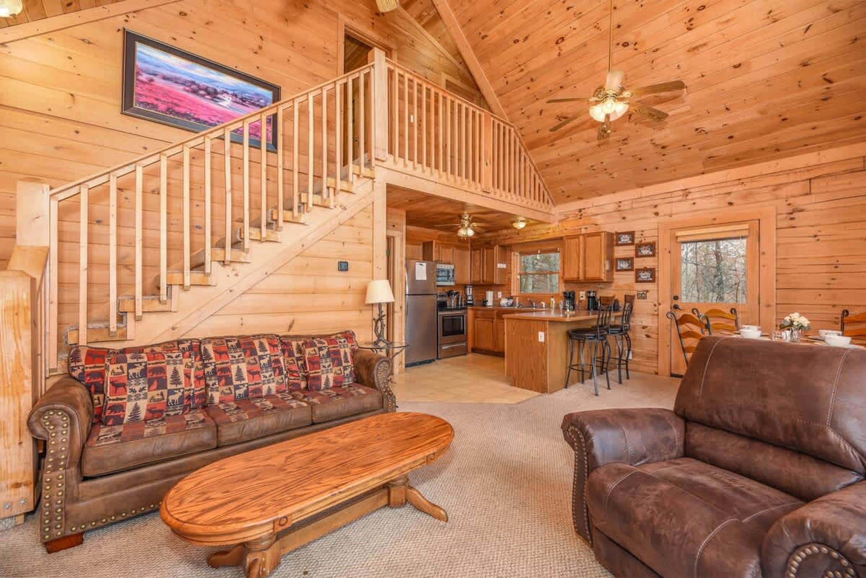 L’intérieur d’un chalet en bois comprend un escalier, un canapé, une table basse, un coin cuisine et une table à manger.