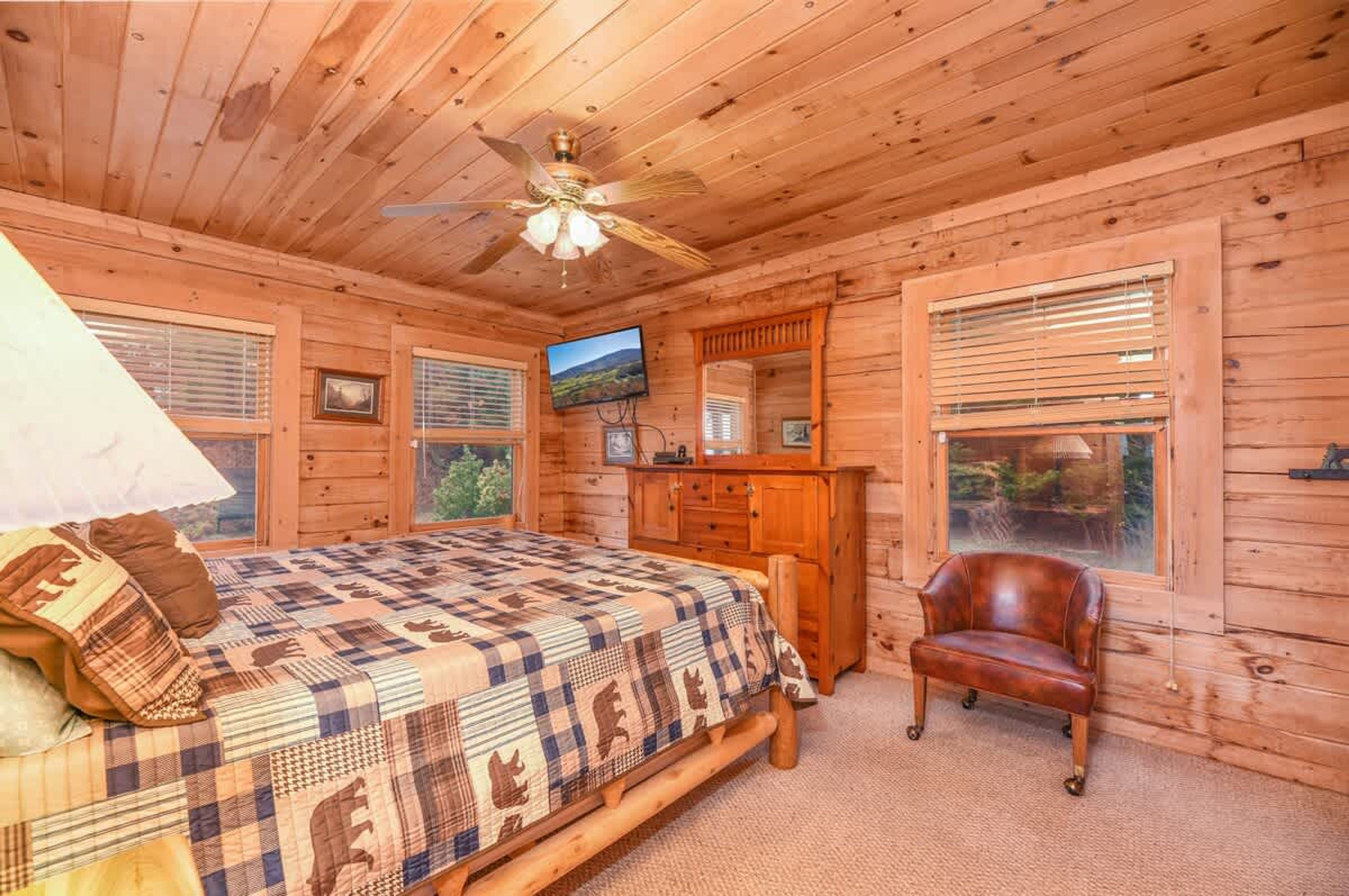 Une chambre dans une cabane en bois, avec un lit, un bureau, une chaise et un ventilateur de plafond.