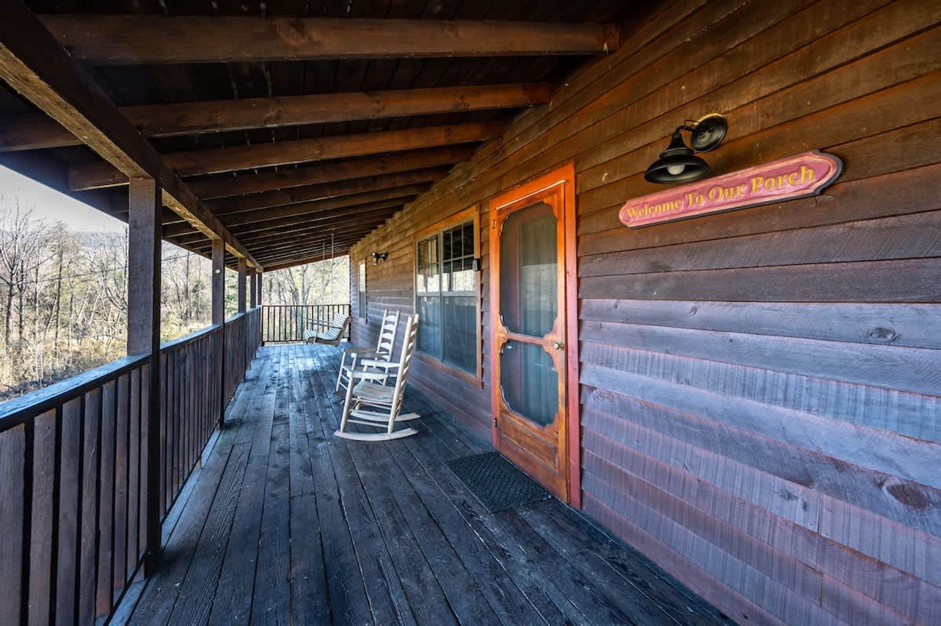 A wooden cabin with a porch, rocking chairs, and a sign welcoming guests.