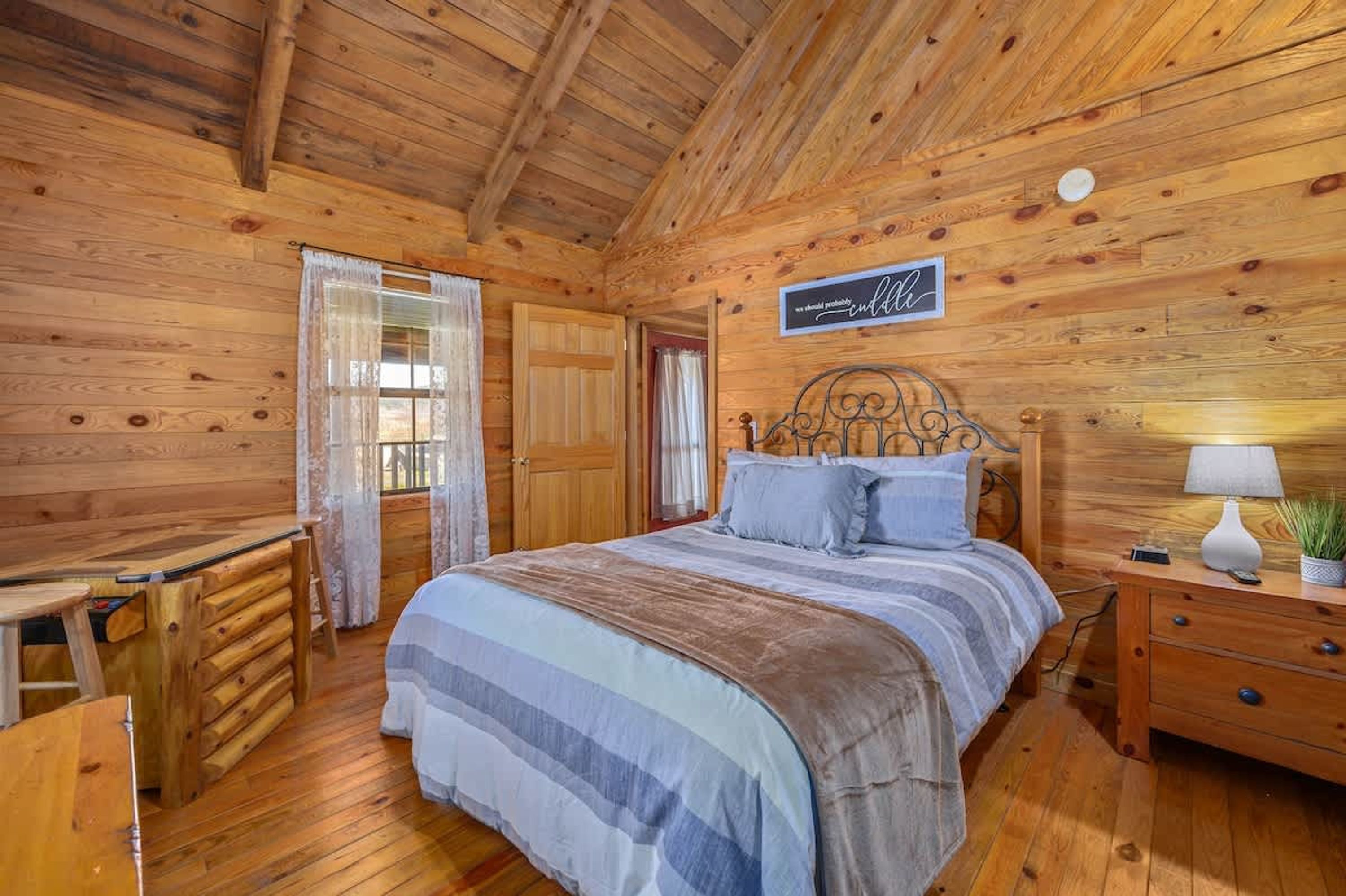 A wooden cabin bedroom with a bed, bedside table, and a desk.