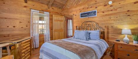 A wooden cabin bedroom with a bed, bedside table, and a desk.