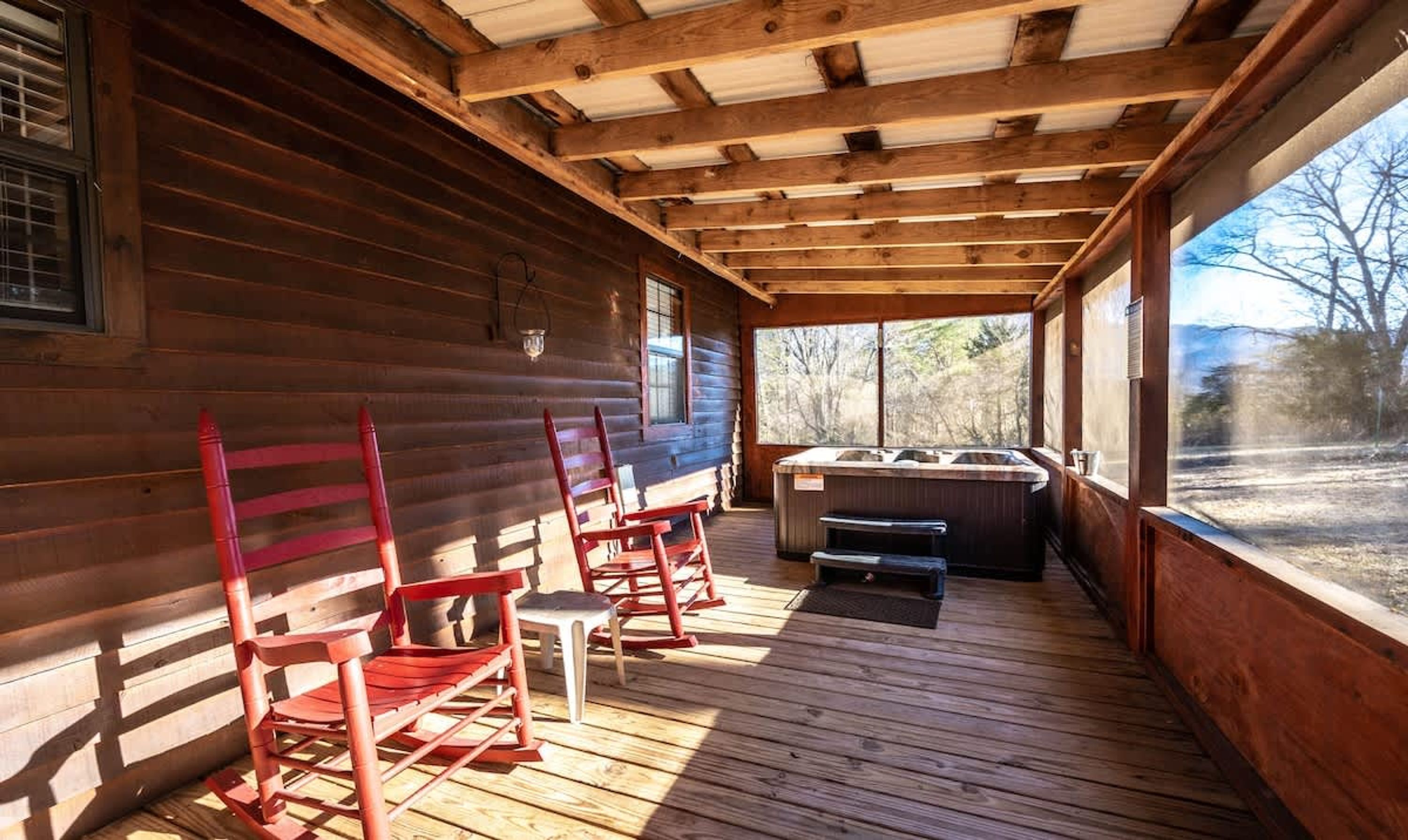 A wooden cabin with a porch, a hot tub, and rocking chairs.