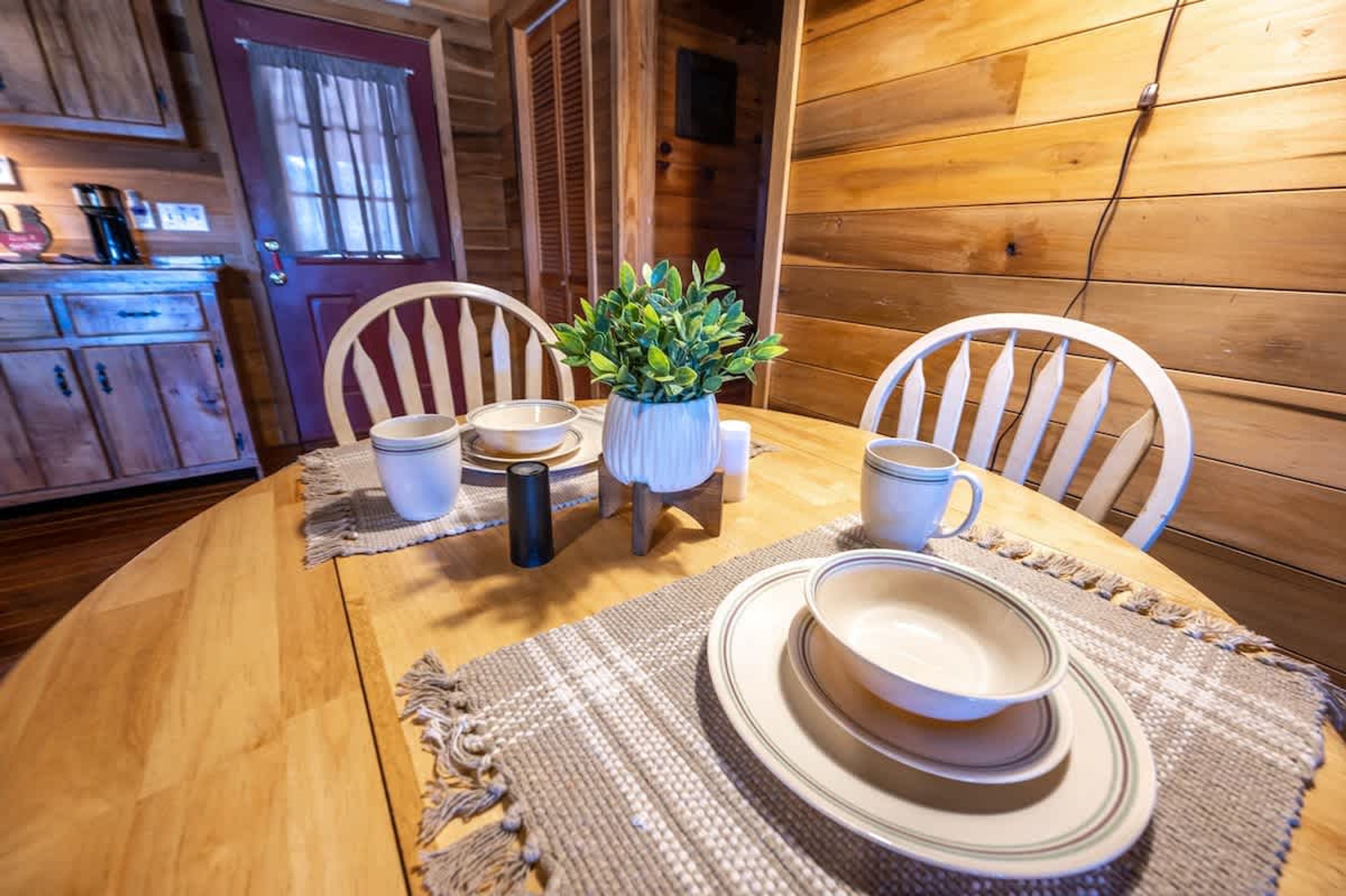 Una mesa de madera para comer dispuesta con platos, tazones y tazas, rodeada de sillas.