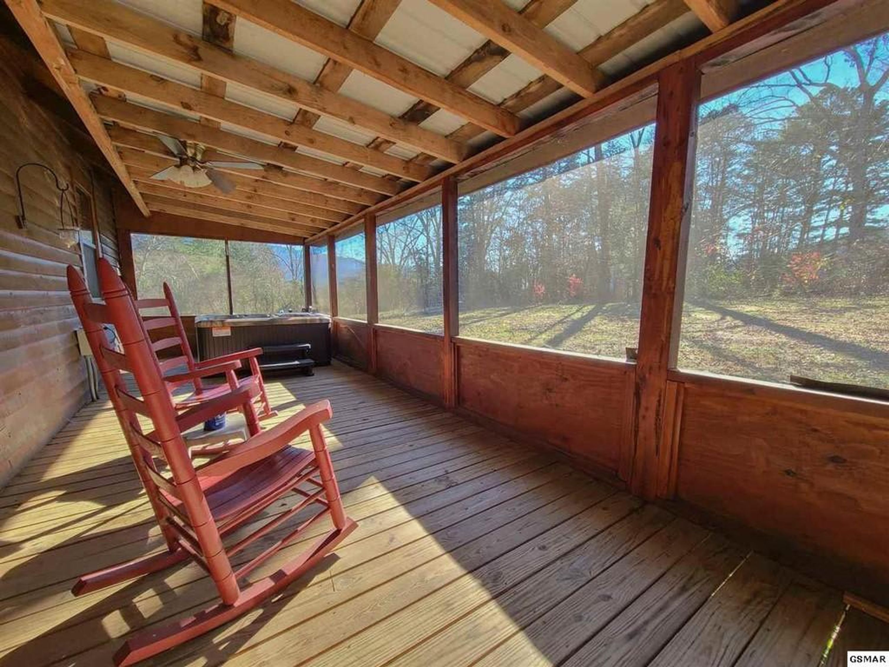 En inglasad veranda med trägolv, en gungstol och ett bubbelbad.