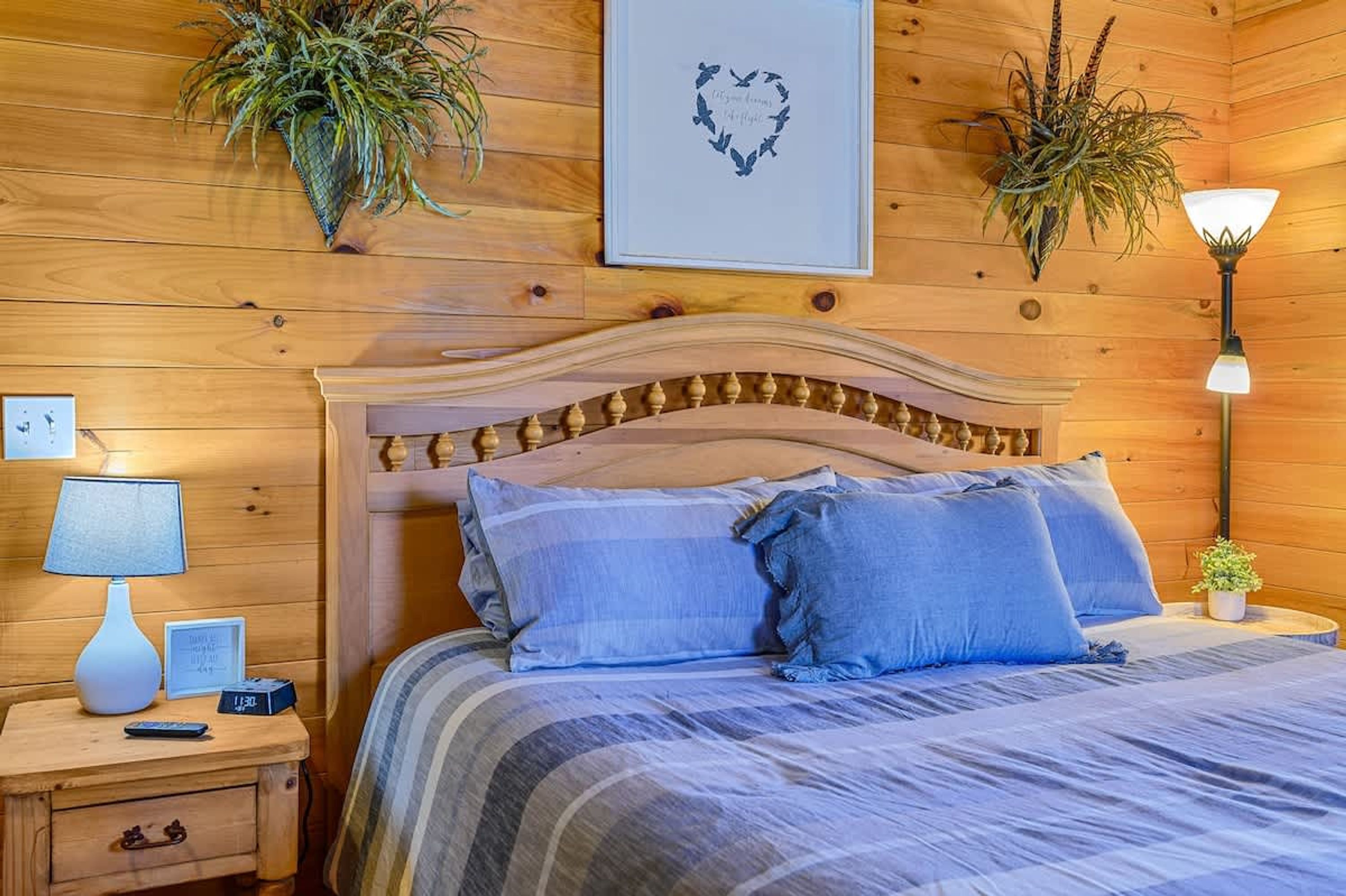 Une chambre à coucher aux murs lambrés, avec un lit, des oreillers, une table de chevet avec une lampe et des plantes fixées au mur.