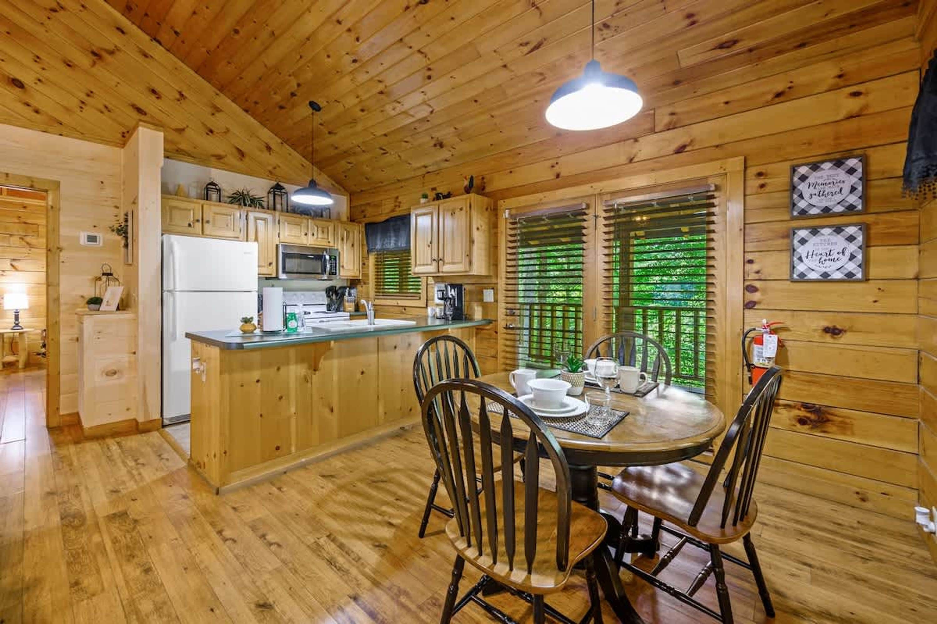 Interior de uma cabana de madeira com cozinha, sala de jantar e uma geladeira visível.