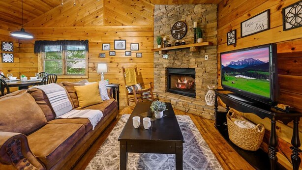 A cozy cabin interior with a wooden ceiling, a stone fireplace, a television, and a sofa. - Location Log Cabin Hot Tub Fireplace Pool Fishing (Sevierville)