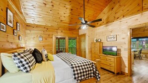A wooden cabin bedroom with a bed, dresser, television, and ceiling fan. - Location Log Cabin Hot Tub Fireplace Pool Fishing (Sevierville)