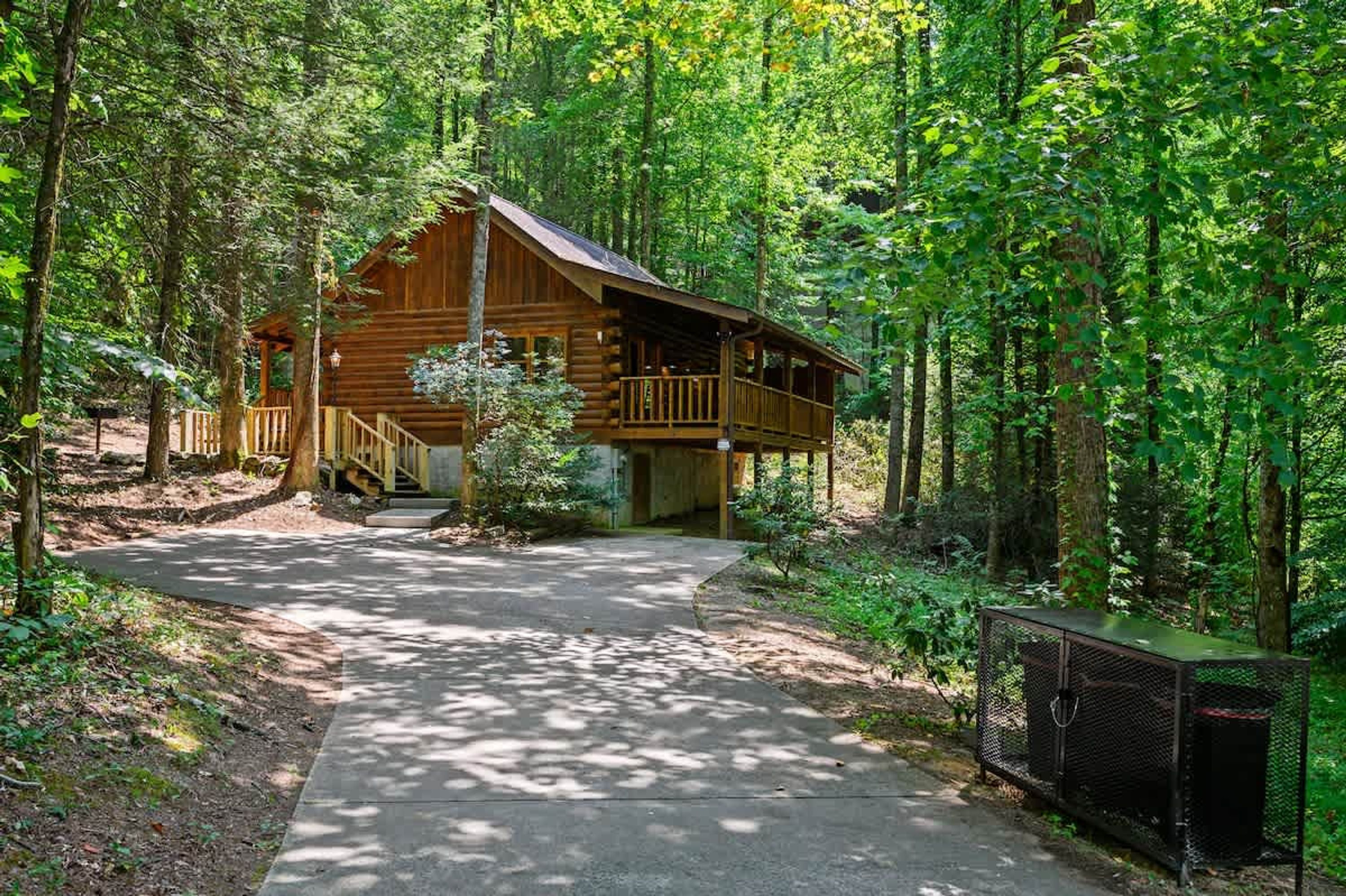 A wooden cabin with a porch and a fenced area, surrounded by dense forest.