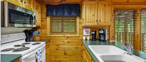 Una cocina con armarios de madera, estufa, microondas y pileta.