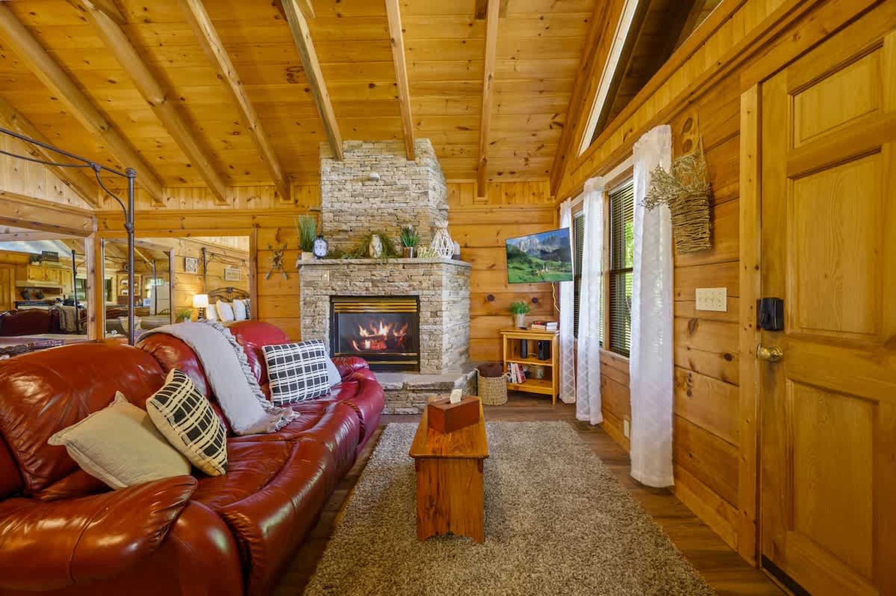 A cozy log cabin interior with a stone fireplace, a red leather couch, and wooden walls.