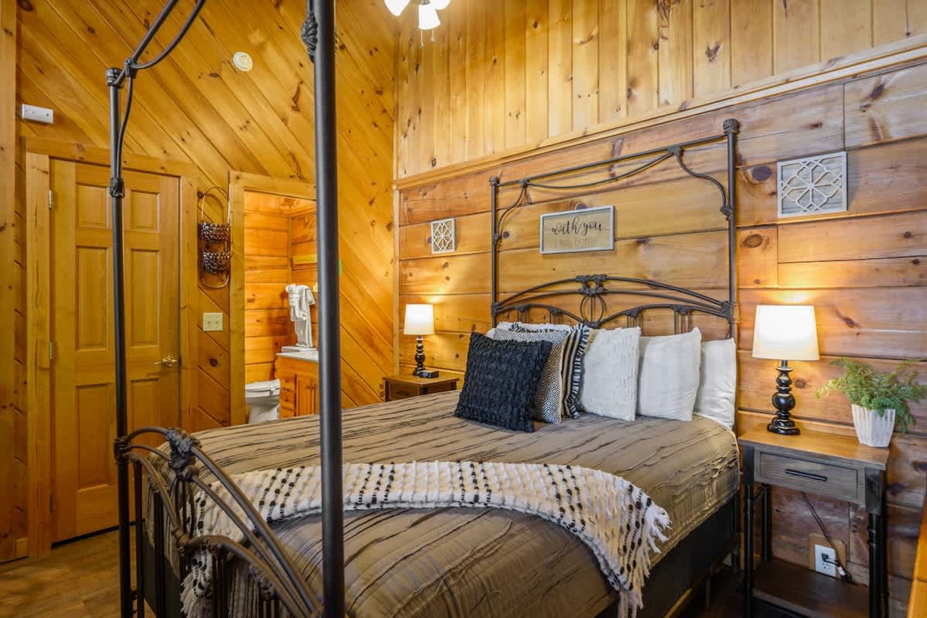 A wooden-paneled bedroom with a four-poster bed, a bedside table with a lamp, and a wall-mounted shelf.