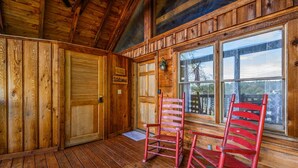 Ein Interieur einer Holzhütte mit Holztür, einem Fenster mit Jalousien und zwei roten Stühlen.