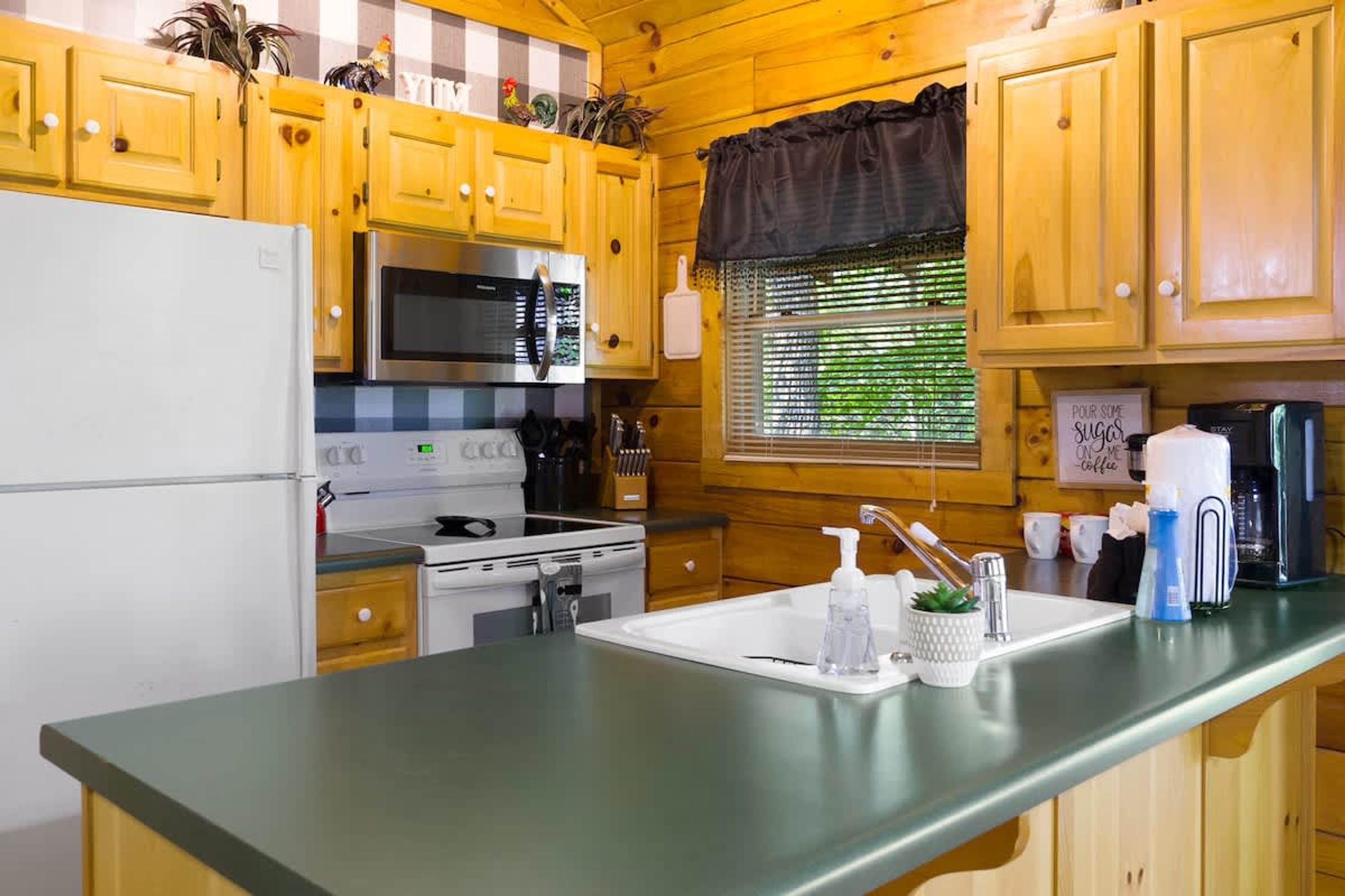 A kitchen with wooden cabinets, a refrigerator, a microwave, an oven, a sink, and a window with blinds.
