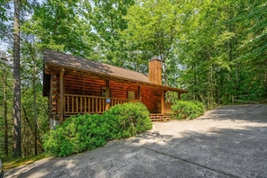 A rustic log cabin with a chimney, surrounded by dense green foliage and a paved driveway. - Location Log Cabin Hot Tub Fireplace Pool Fishing (Sevierville)