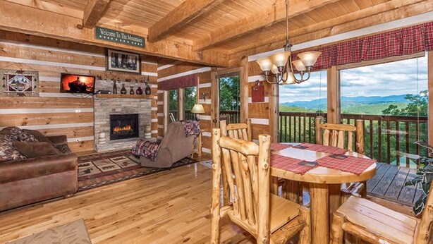 A cozy cabin interior with a fireplace, wooden furniture, and a scenic outdoor view. - View Private Hot Tub Pool Table Fireplace Relax (Sevierville)