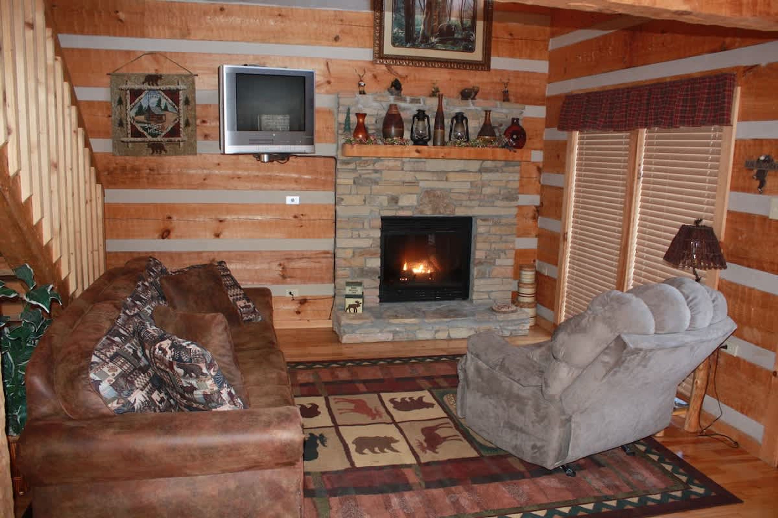 A cozy log cabin interior with a stone fireplace, leather sofas, and a television.