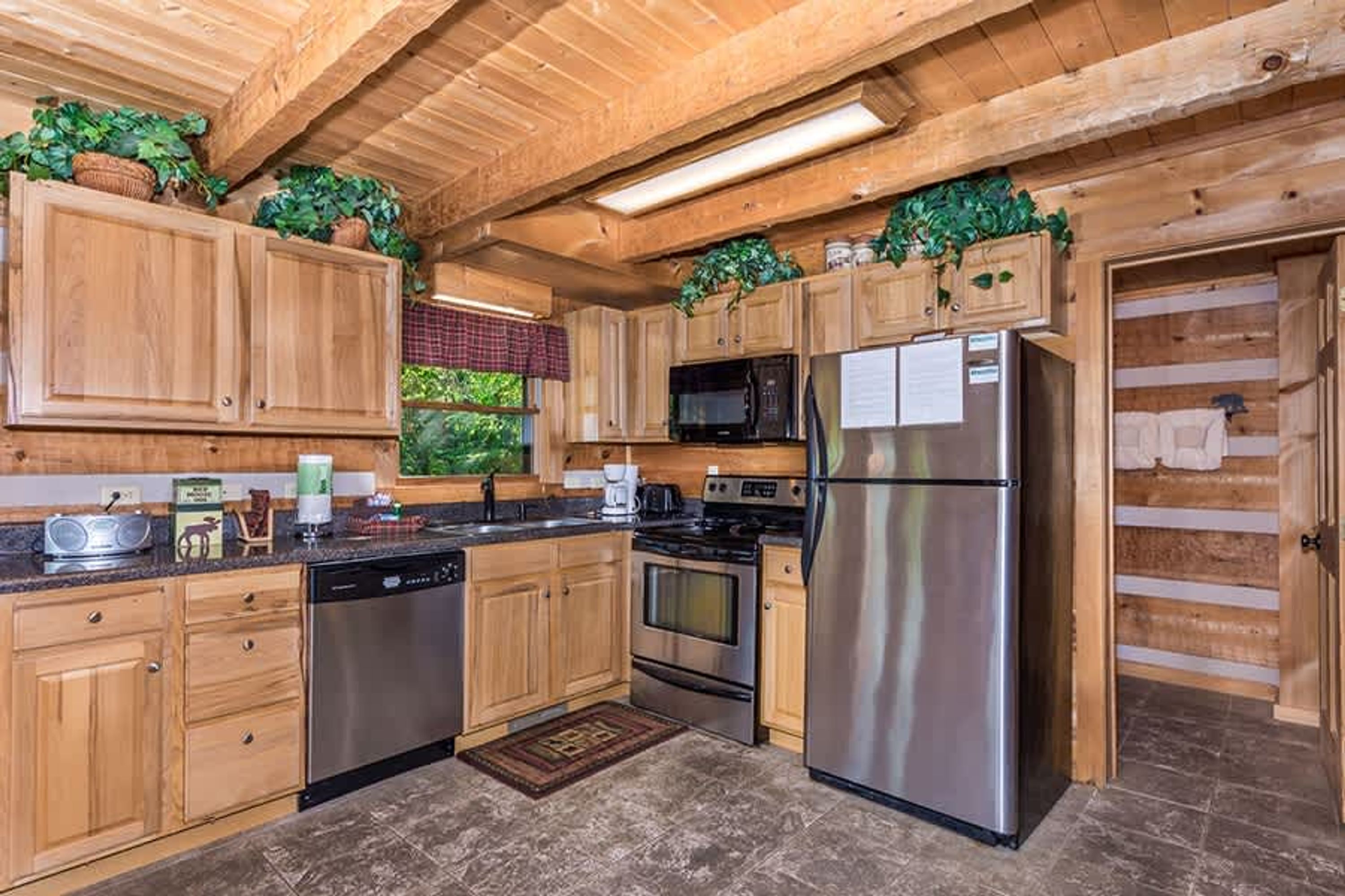 A modern kitchen with wooden cabinets, stainless steel appliances, and a window with a view of greenery.