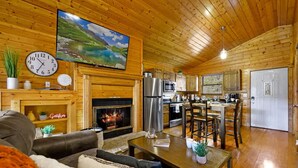 A cozy cabin interior with a fireplace, wooden walls, a dining area, and a kitchen. - Great View Location Studio Log Cabin Hot Tub (Gatlinburg)