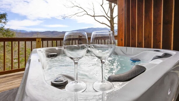 A hot tub with two glasses of water on a wooden deck with a mountain view. - Great View Location Studio Log Cabin Hot Tub (Gatlinburg)