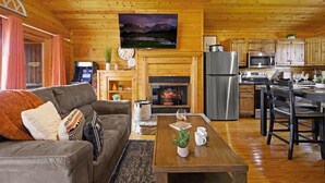 A cozy cabin interior with a living room, fireplace, kitchen, and a television mounted above the fireplace. - Great View Location Studio Log Cabin Hot Tub (Gatlinburg)
