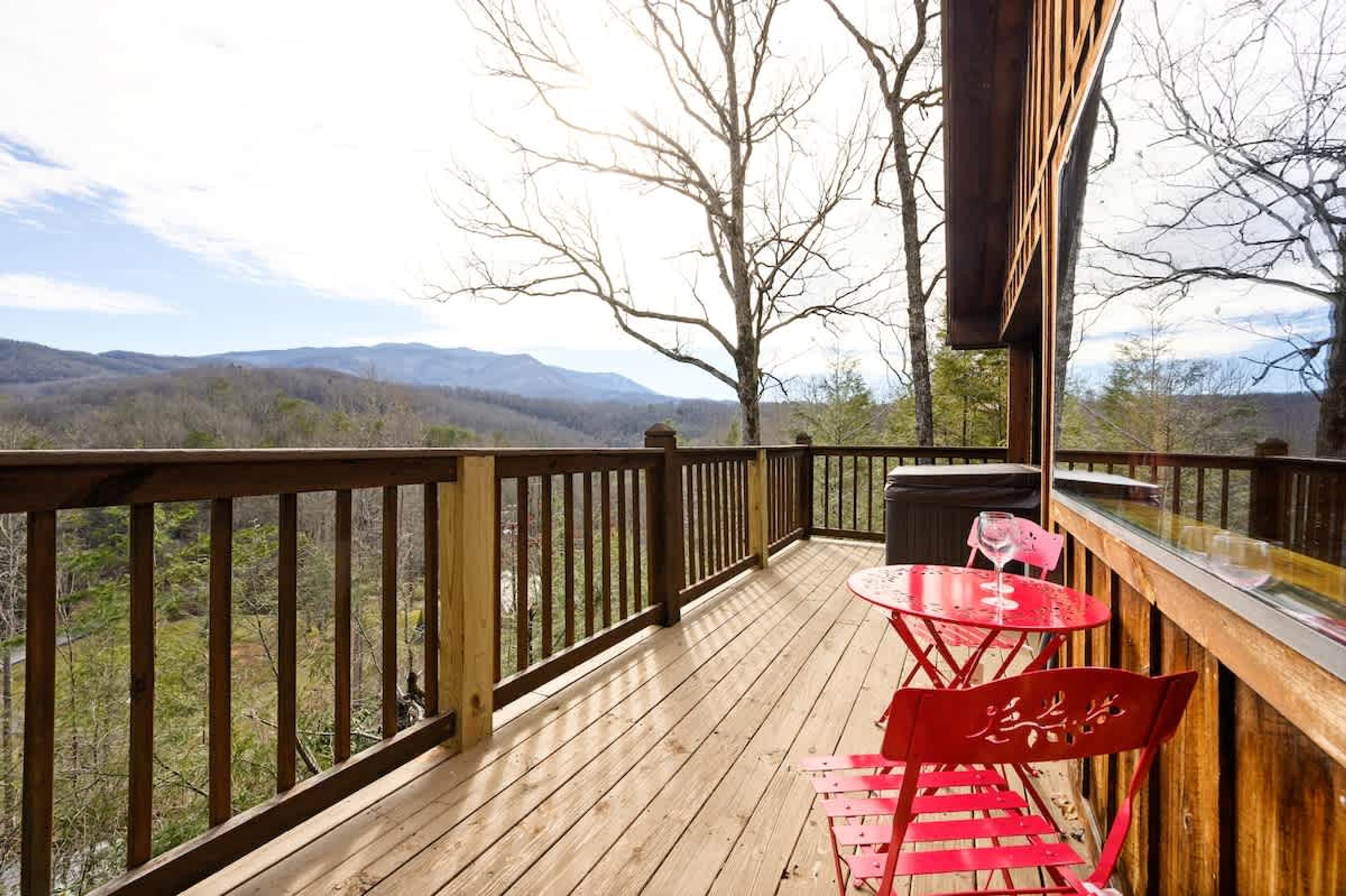 A wooden deck with a table and chairs, overlooking a mountainous landscape.