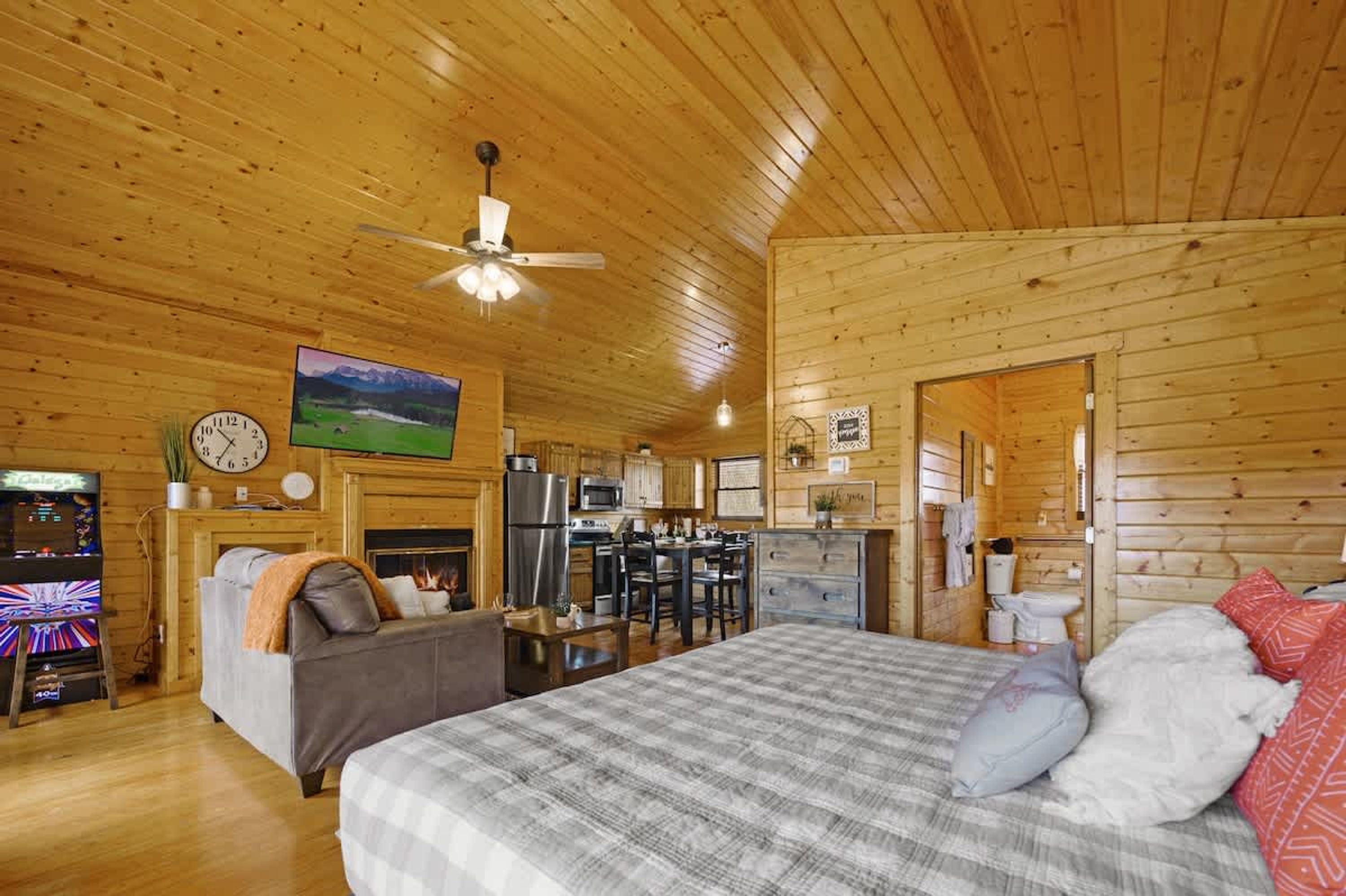 L’intérieur d’un chalet confortable en bois, avec un grand lit, une cheminée, un coin repas et une cuisine.
