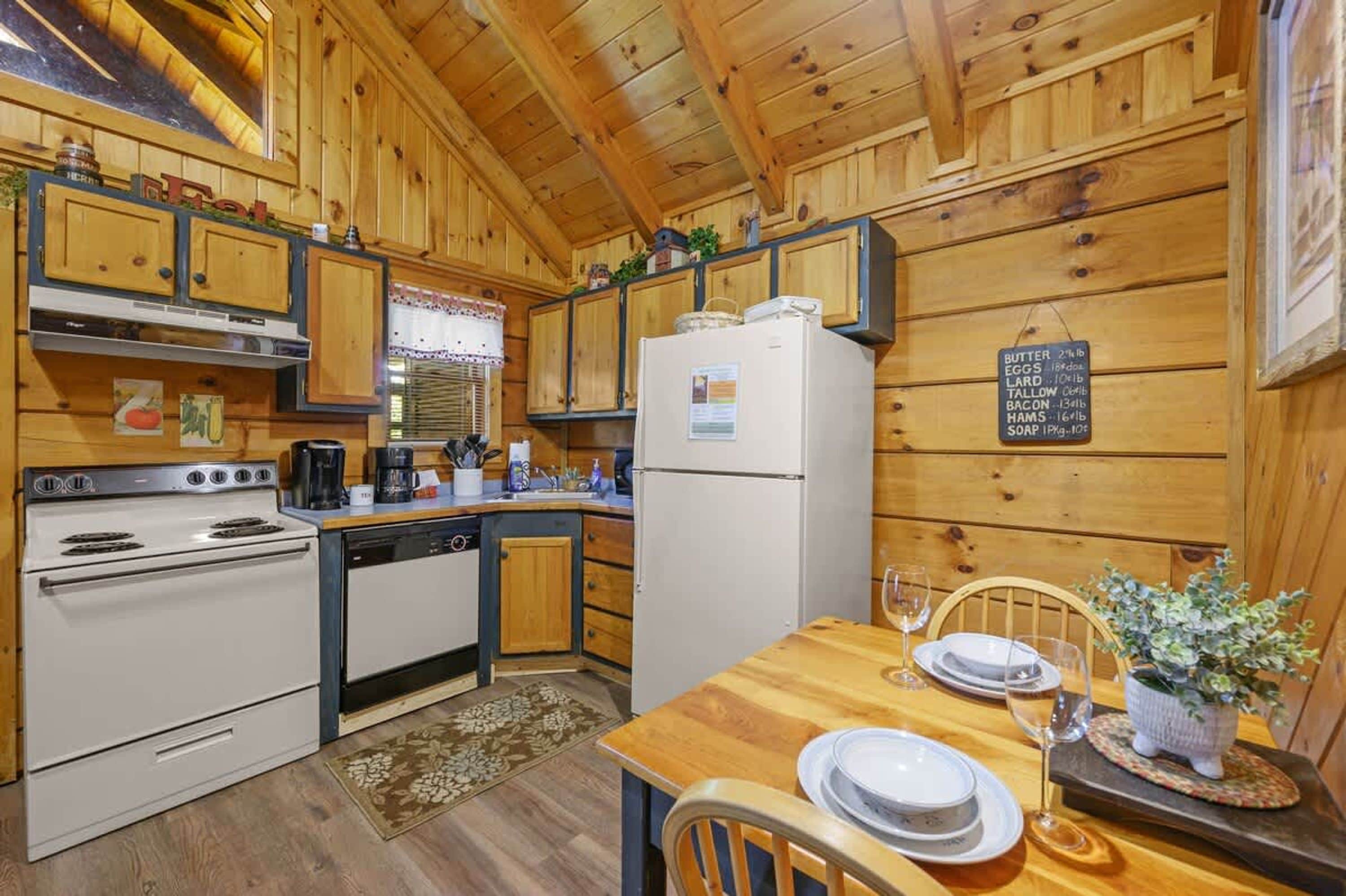 A wooden cabin kitchen with a stove, refrigerator, and dining table set for two.