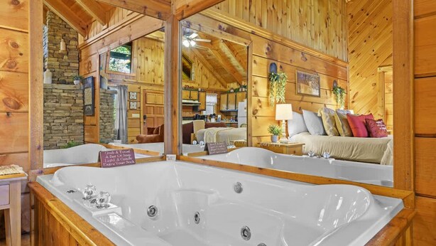 Interieur van een houten chalet met een groot bad, een stenen open haard en een gezellige zithoek met een bank en kussens.