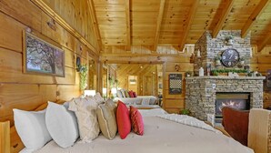 Een knus houten blokhutinterieur met een stenen openhaard, een bed met kussens en houten wanden.