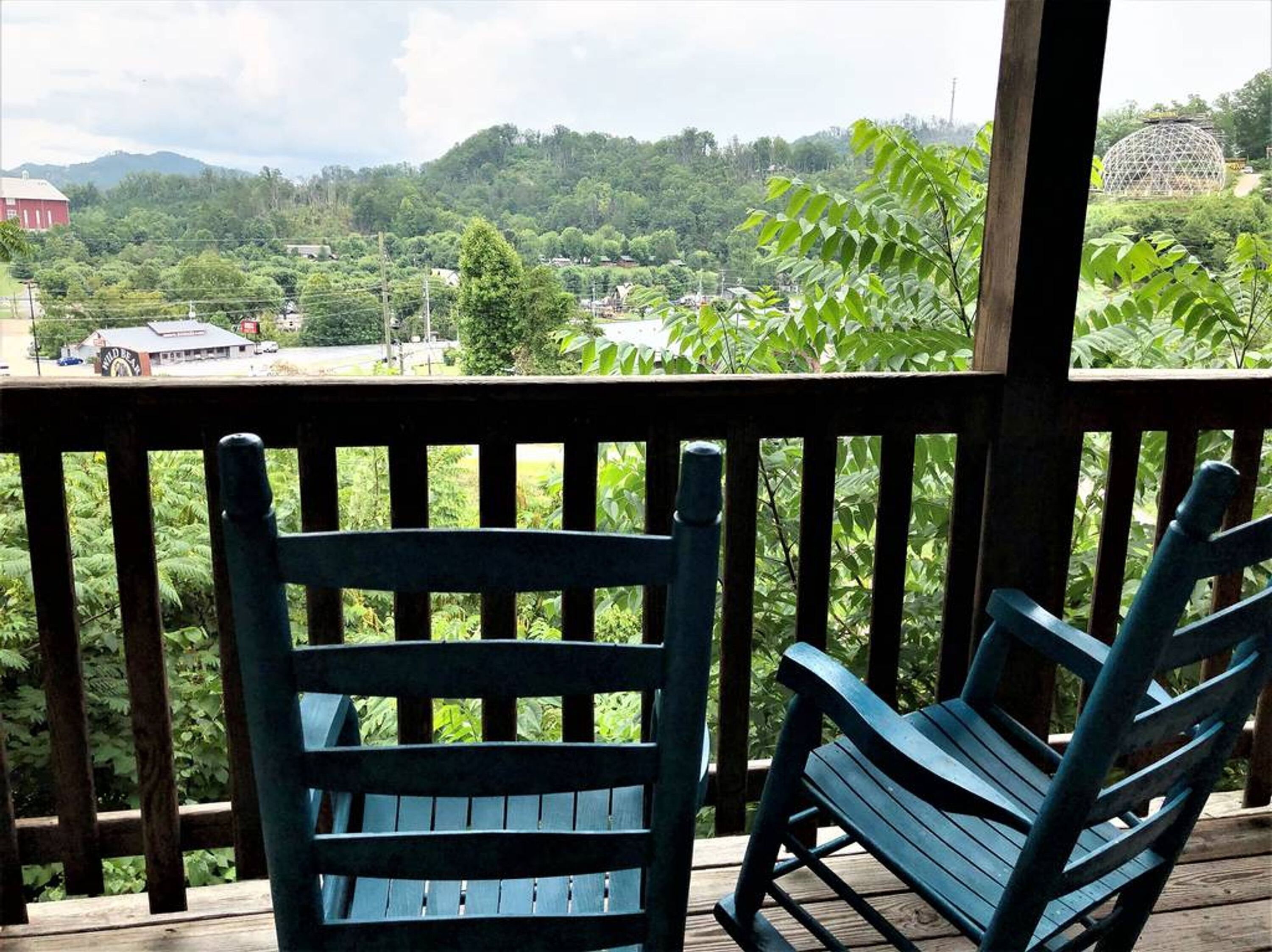 A wooden deck with two blue chairs overlooking a lush landscape with a dome-shaped structure in the distance.