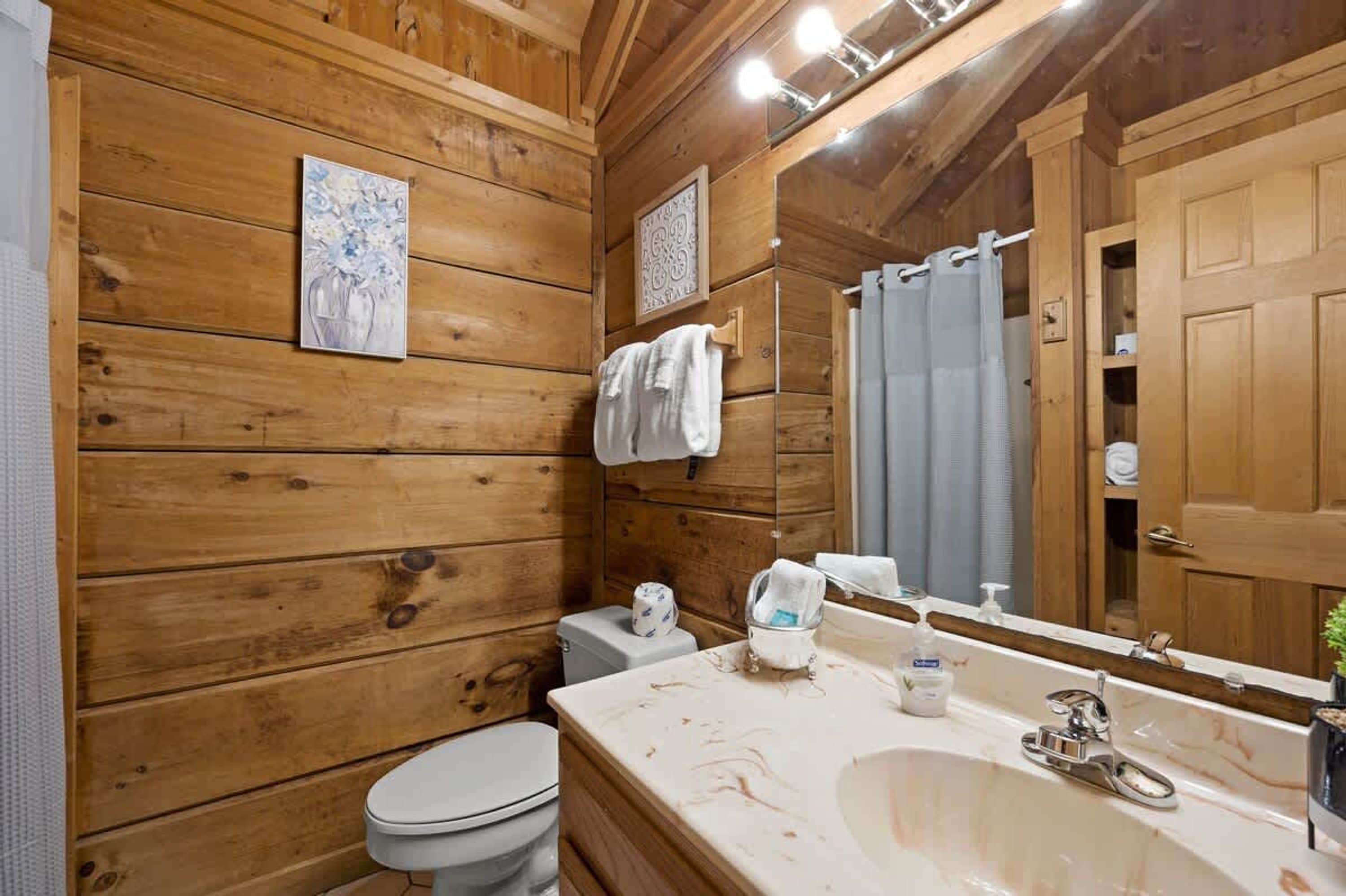 Baño de cabaña de madera con inodoro, lavamanos y espejo.